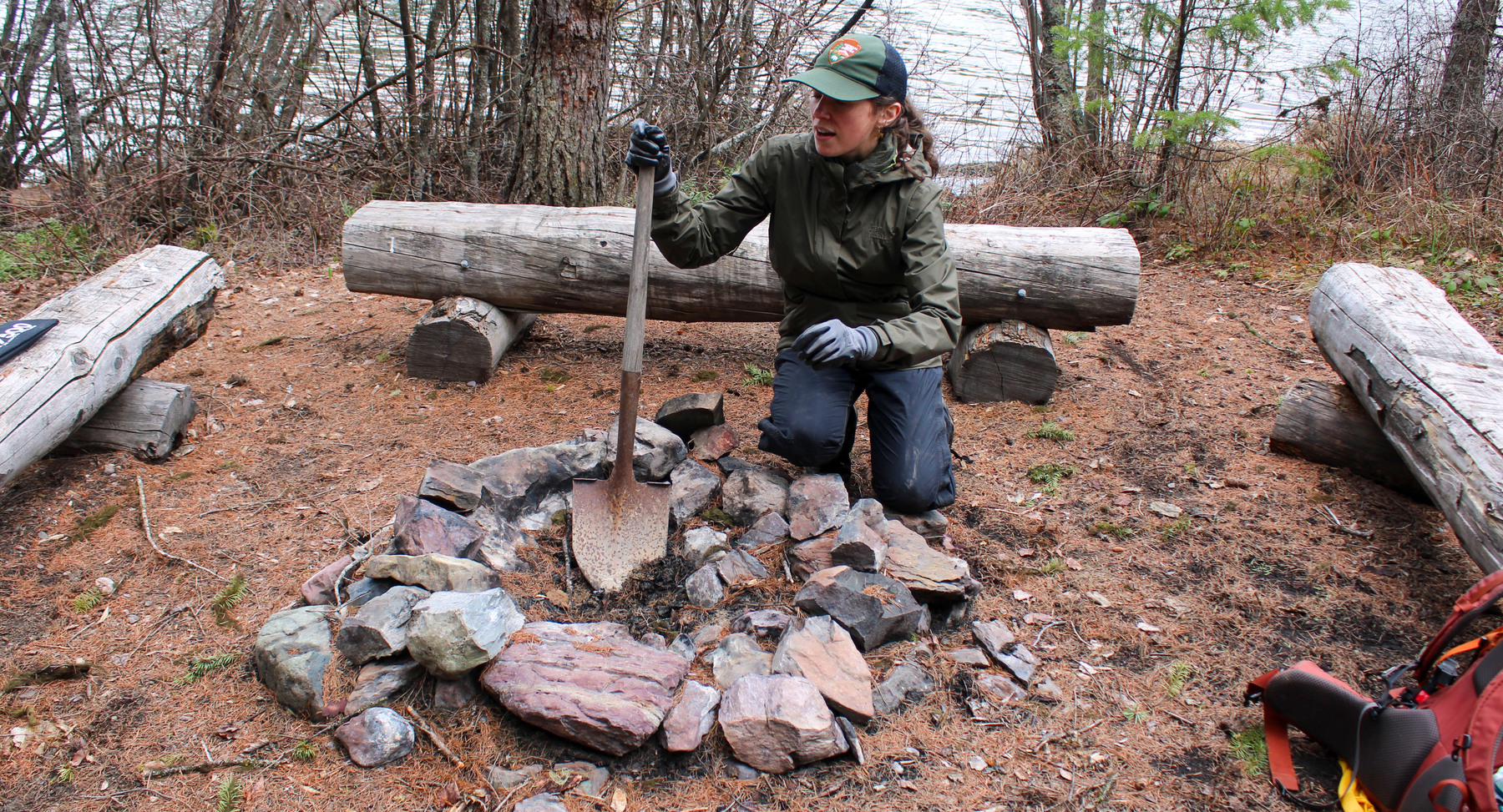 A ranger cleans a fire pit.