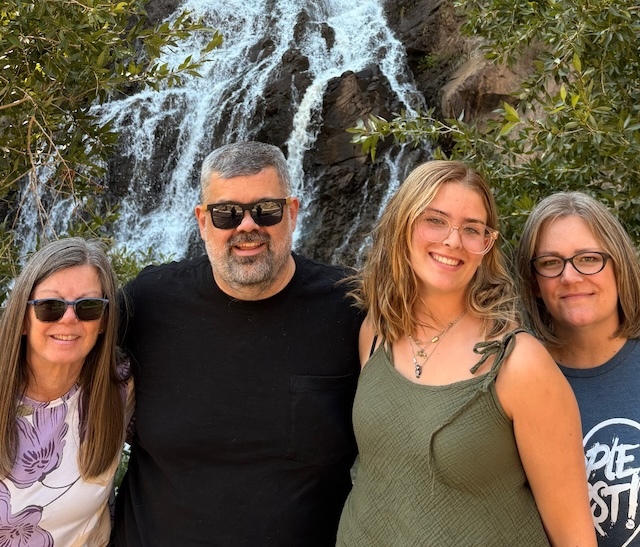 Angie with her husband, daughter, and mother in law in front of a waterfall in Utah, Summer 2025.